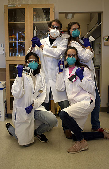 Four students posing with lab coats and masks.